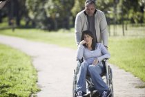 Uomo spingendo donna in sedia a rotelle nel parco — Foto stock