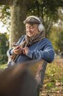 Senior man on park bench with cell phone and headphones — Stock Photo