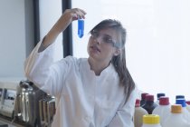 Química joven mirando reactivo en un laboratorio químico - foto de stock