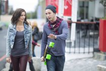 Pareja joven caminando en la ciudad, hombre sosteniendo longboard - foto de stock