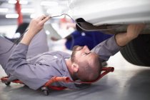 Meccanico auto su carrello raccoglitore al lavoro in garage di riparazione — Foto stock