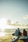 Drei Teenager sitzen bei Sonnenuntergang am Strand — Stockfoto