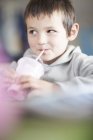 Retrato del niño sonriente bebiendo batido en la cafetería - foto de stock