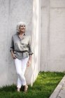 Femme âgée aux cheveux blancs souriants appuyée contre un mur en béton — Photo de stock
