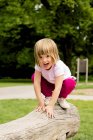 Menina no playground agachado no log — Fotografia de Stock