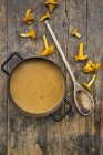 Cooking pot of cream of chanterelle soup, wooden spoon and chanterelles on dark wood — Stock Photo