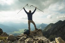 Österreich, Tirol, Tannheimer Tal, Junger Mann mit Wanderstöcken jubelt auf Berggipfel — Stockfoto