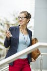 Smiling young businesswoman with smartphone and briefcase walking on staircase — Stock Photo