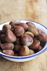 Enamel bowl of sweet chestnuts on wooden surface — Stock Photo