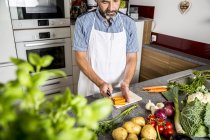 Austria, Man in kitchen chopping carrots — Stock Photo