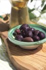 Bowl of black olives on board made of olive wood — Stock Photo