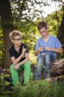 Dois meninos sentados em um tronco de árvore cortando uma maçã com uma faca de bolso — Fotografia de Stock