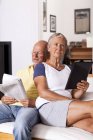 Старший пара, сидячи на дивані, читати газети і за допомогою цифровий планшетний — стокове фото