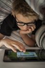 Niño acostado en la cama usando tableta digital - foto de stock