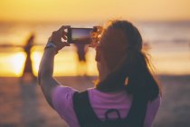 Donna sulla spiaggia fotografare il tramonto con il suo smartphone — Foto stock