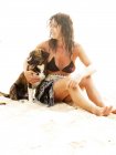 Mulher vestindo top biquíni sentado com cão na praia de areia — Fotografia de Stock
