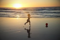 Хлопчик працює на пляжі на заході сонця — стокове фото