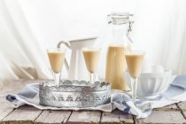 Trois verres et une bouteille de liqueur d'oeuf maison placés sur une table en bois avec bol d'oeufs — Photo de stock