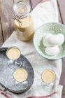 Elevated view of three glasses and bottle of homemade egg liqueur placed on wooden table with bowl of eggs — Stock Photo