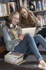 Дві студентки, сидячи в бібліотеки, що дивлячись на цифровий планшетний — стокове фото