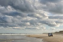 Австралия, Новый Южный Уэльс, Потсвилл, внедорожник, стоящий на пляже с серфингом и темными облаками — стоковое фото
