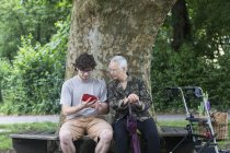 Femme âgée regardant jeune homme avec tablette numérique sur banc de parc — Photo de stock