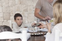 Familia almorzando en la mesa del comedor con niño entregando la tableta digital a la madre - foto de stock