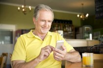 Retrato de homem sênior usando smartphone em um café — Fotografia de Stock