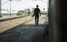 Jeune homme avec planche à roulettes marchant sur la plate-forme ferroviaire — Photo de stock