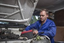Man working on car in home garage removing battery — Stock Photo