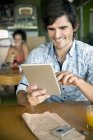 Retrato del hombre sonriente usando tableta digital en un café - foto de stock