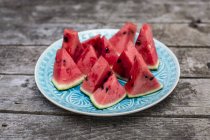 Gehackte Wassermelone auf blauem Teller auf dunklem Holz — Stockfoto