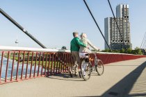 Alemania, Mannheim, Pareja madura cruzando el puente, empujando la bicicleta - foto de stock