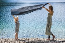 Austria, Tyrol, Lake Plansee, mother and daughter holding cloth at lakeshore — Stock Photo