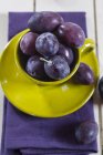 Frische Pflaumen in grüner Tasse auf Untertasse auf violetter Serviette — Stockfoto