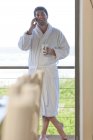 Jovem vestindo roupão de banho falando no celular na casa de praia — Fotografia de Stock