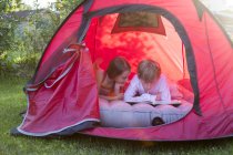 Garçon et fille lisant couché dans une tente rouge avec un livre — Photo de stock