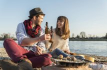 Lächelndes Paar trinkt Bier am Flussufer — Stockfoto