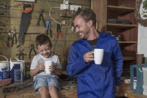 Father and son working in home garage having coffee break — Stock Photo