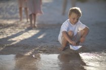 Boy playing with paper boat at a water pool on a sandy beach — Stock Photo