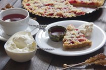 Полуничний рум'яний пиріг зі збитими вершками та чашкою фруктового чаю з шматочком на тарілці — стокове фото