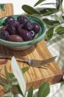 Bowl of black olives and fork on board made of olive wood — Stock Photo