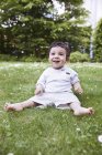 Baby boy sitting on grass and holding daisy flower, smiling — Stock Photo