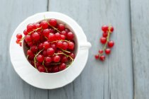 Fresh redcurrants in cup on wooden surface — Stock Photo