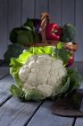 Cauliflower with basket of fresh vegetables on grey wooden table — Stock Photo
