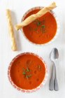 Cold bell pepper soup in bowl with bread sticks on white surface — Stock Photo