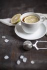 Xícara de chá com fatia de limão, açúcar de rocha e coador de chá na mesa de madeira, tiro estúdio — Fotografia de Stock