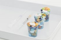 Cup overfull with pills over white tray — Stock Photo