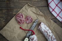 Sliced Italian salami on parchment with knife — Stock Photo