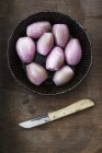 Kitchen knife and peeled shallots in a bowl on wooden table, studio shot — Stock Photo